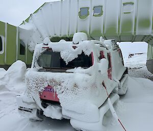 A pink vehicle is parked, and covered in snow