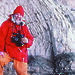 Expeditioner holding two cameras; a rock face in the background