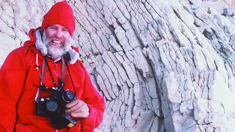 Expeditioner holding two cameras; a rock face in the background