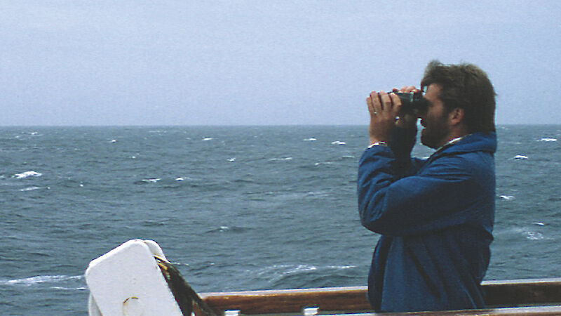 An expeditioner looks through binoculars for seabirds, from the vessel ‘Polar Bird'