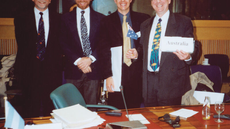 Four people in suits stand behind a desk.