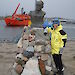 Female expeditioner posing next to statue of Mawson at the station, with icebreaker in the background