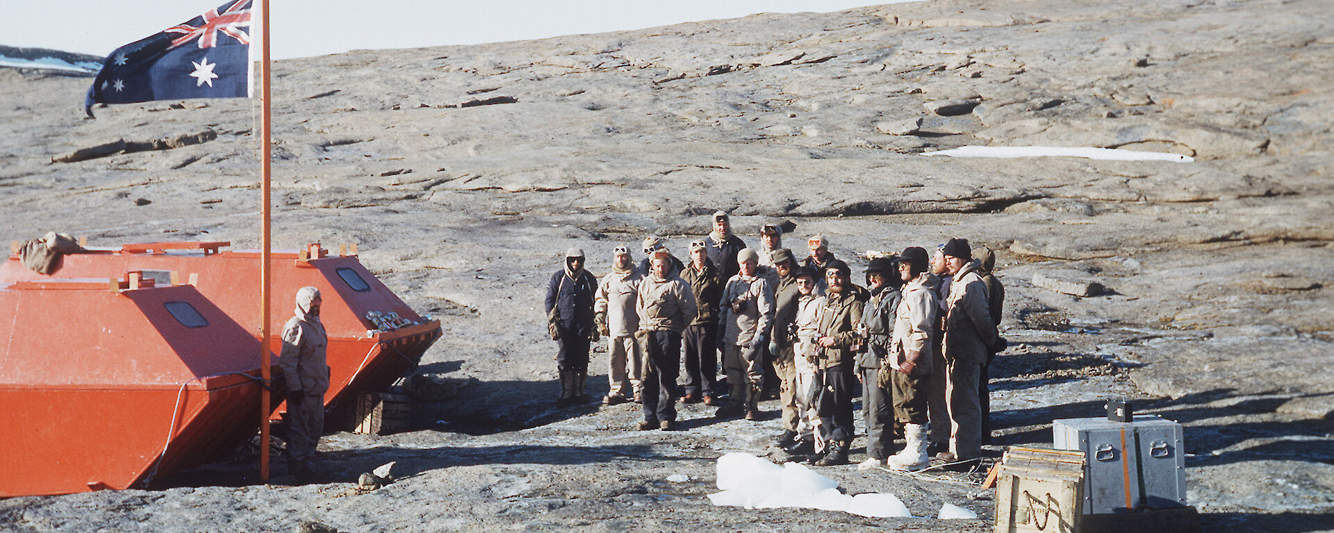 Phil Law stands at the foot of the flagpole, raised on 13 February 1954 at the establishment of Mawson station