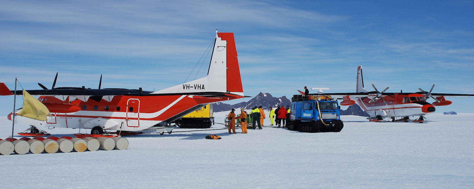 A C212 aircraft and hagglund surrounded by fuel drums.