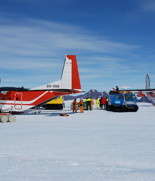 A C212 aircraft and hagglund surrounded by fuel drums.