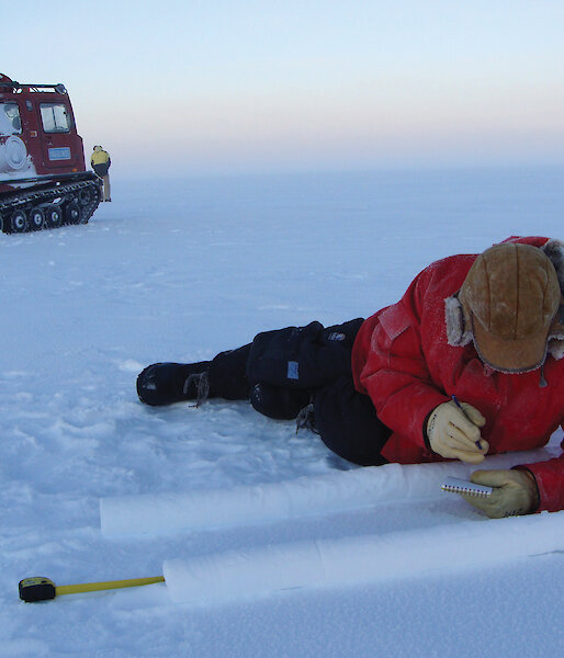 Ice core chemist lying on the ice, cataloguing ice cores, with vehicle in background