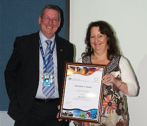 Man and woman pose for photograph, woman is holding a framed certificate