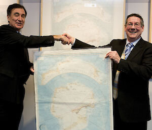 Two men shaking hands, one presents an old Antarctic map