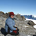 Lynette Finch seated on rocky ground with penguins and icebergs in the background