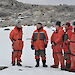Dr Tony Press and three others, standing in orange Antarctic freezer suits, receive a briefing from a scientist at Casey station