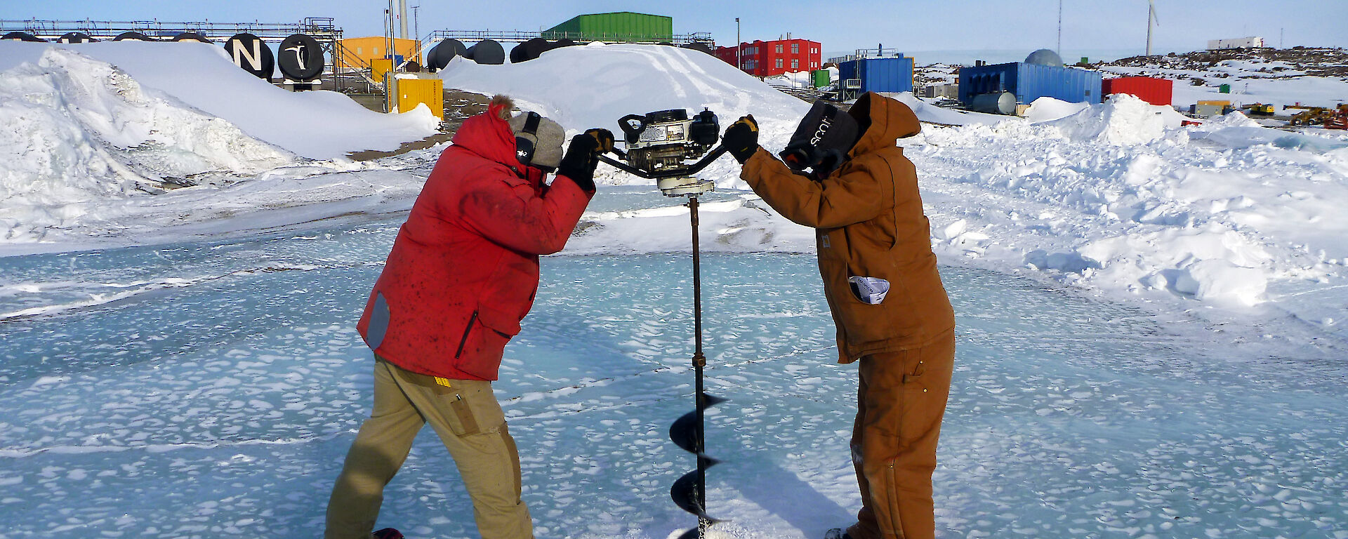 Two scientists drilling a hole in the sea ice.