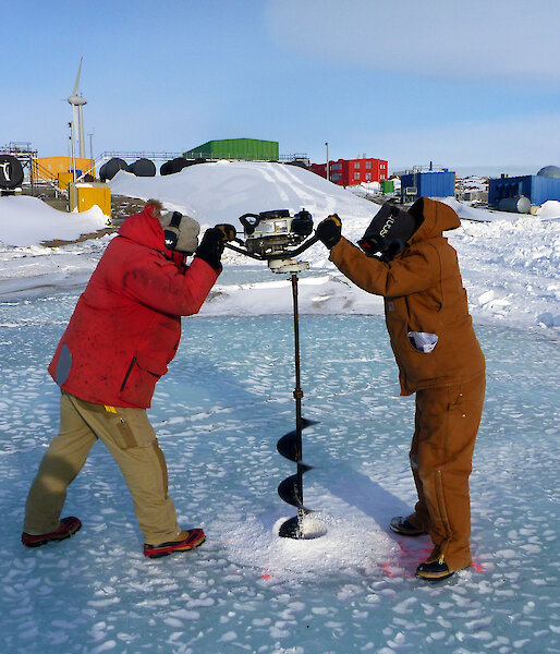 Two scientists drilling a hole in the sea ice.