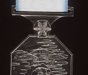 On the reverse of the medal is a depiction of an expeditioner walking in to drifting snow, with Mawson’s Hut in the background.