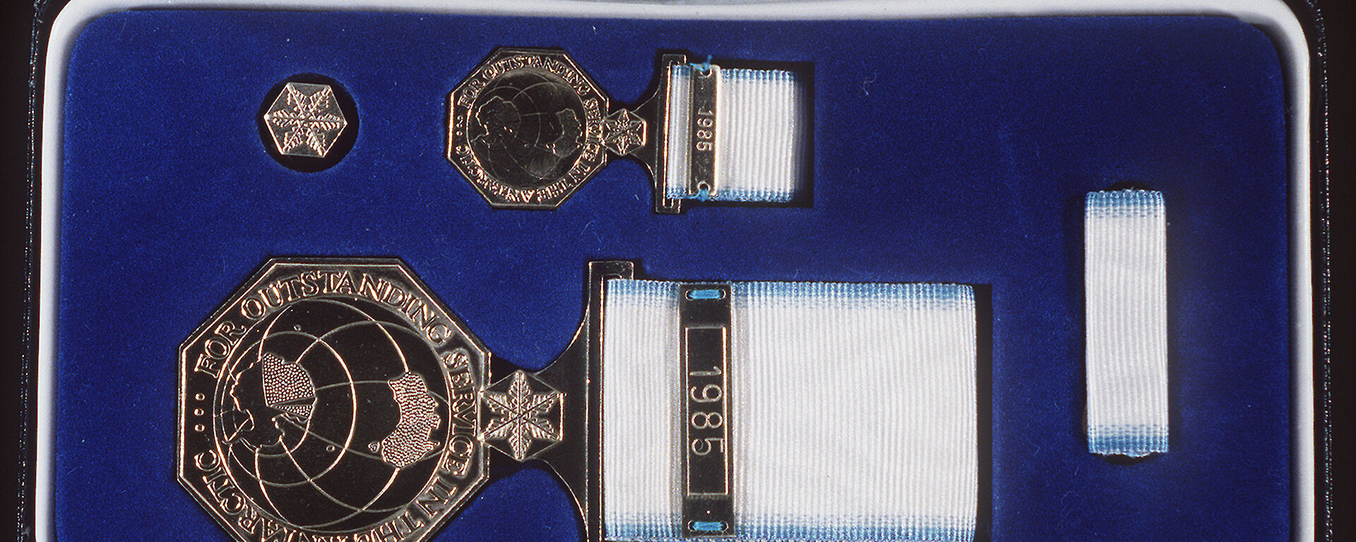The Australian Antarctic Medal is presented in a box containing: a ‘ribbon bar’, for those in the uniformed services to wear on their uniforms; a miniature medal for wearing with formal evening dress; a lapel badge for everyday wear; and the full-sized medal for wearing on appropriate occasions during the day. The full sized medal has the recipient’s name stamped on the rim.