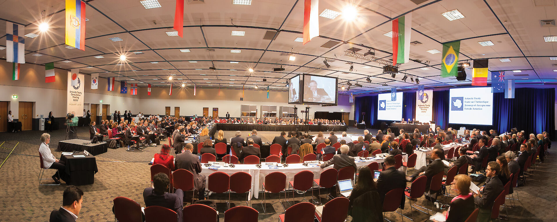 Treaty meeting delegates in the large meeting room decorated with the flags of treaty nations.