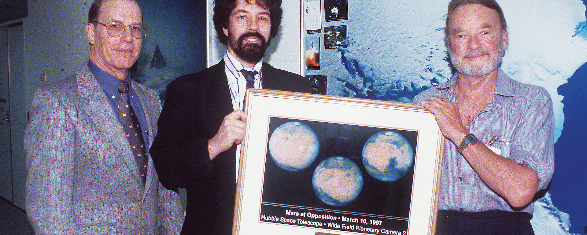 Dr Duane Pierson, Director of Microbiology at NASA JSC (left), and Dr Marc Shepanek of the Office of the Chief Health & Medical Officer at NASA HQ, present a picture of the Mars north polar cap to Dr Peter Gormly (right) in 1998