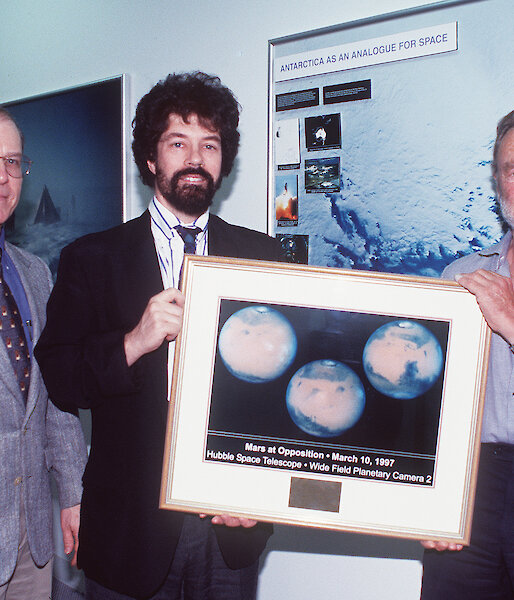Dr Duane Pierson, Director of Microbiology at NASA JSC (left), and Dr Marc Shepanek of the Office of the Chief Health & Medical Officer at NASA HQ, present a picture of the Mars north polar cap to Dr Peter Gormly (right) in 1998