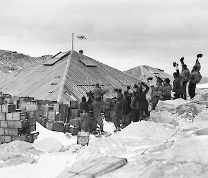 AAE expeditioners raise the flag after completion of the Main Hut at Commonwealth Bay, 1912.