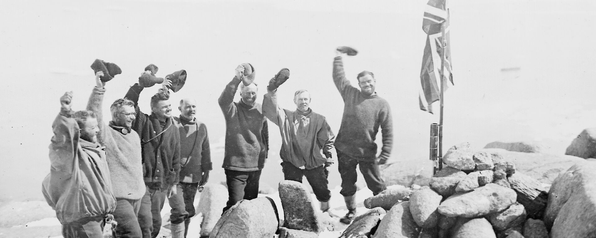 Mawson and his men stand around a rocky cairn with the British flag