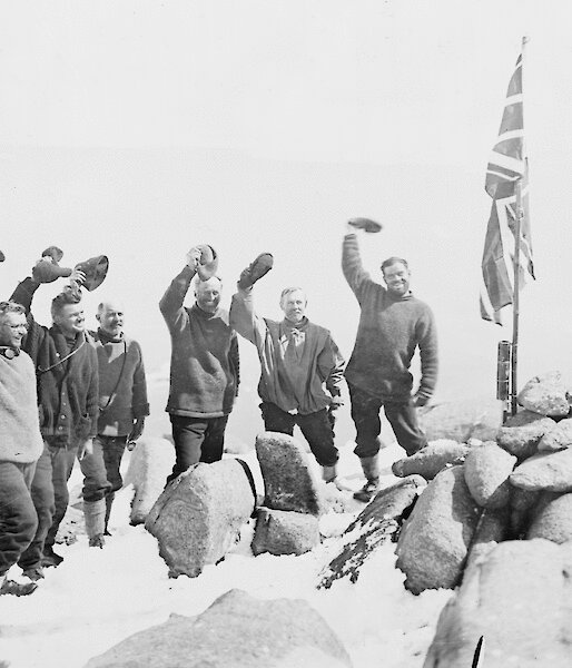 Mawson and his men stand around a rocky cairn with the British flag