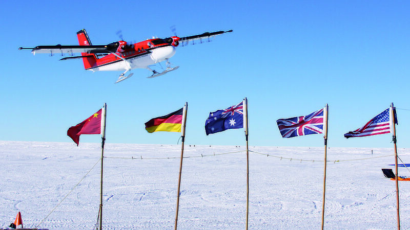 A Twin Otter flies over flags of countries participating in Antarctica’s Gamburtsev Province project.