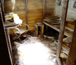 Mawson’s private cubicle showing his bunk, chair and a pile of magazines, all ice-covered, inside the Main Hut.
