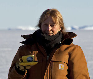 Davis Station Leader, Alison Dean outside in Antarctica holding a cup of tea and saucer