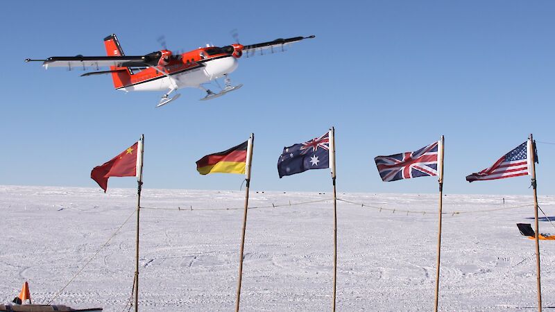 A Twin Otter flies over the flags of countries participating in AGAP.