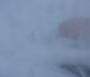 Expeditioner barely discernable outside, moving between huts in the blizzard