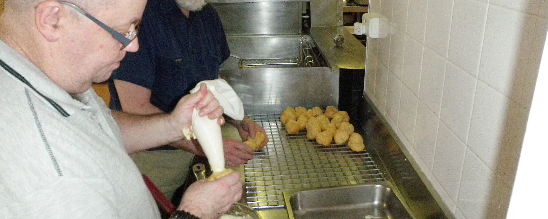 Chef and assistant filling choux balls with custard