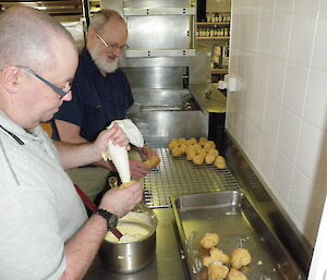 Chef and assistant filling choux balls with custard