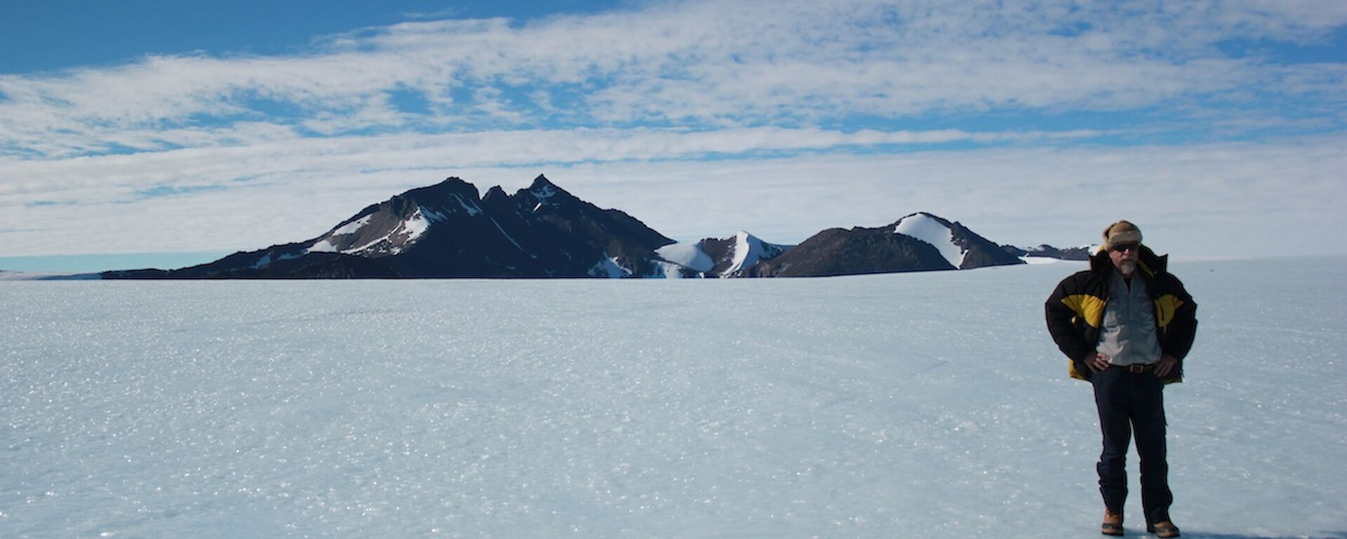 Expeditioner Lloyd standing on the ice plateau with Mt. Henderson in the background