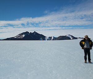 Expeditioner Lloyd standing on the ice plateau with Mt. Henderson in the background