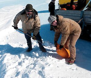 Expeditioners shovelling snow into coloured runway marker bags