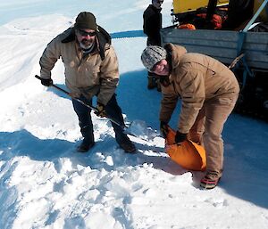 Expeditioners shovelling snow into coloured runway marker bags