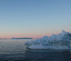 A small ice berg illuminated by the late evening light with the pink and blue sky of sunset in the background