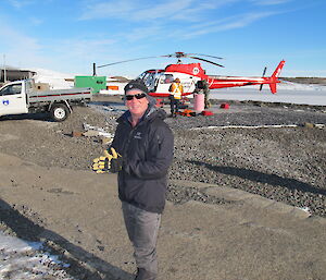 Outgoing Station Leader Mark Williams preparing to leave as pilot refuels helicopter in background.