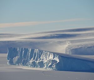 Snow blowing off the ice cliffs to the east of station with grounded iceberg in foreground.