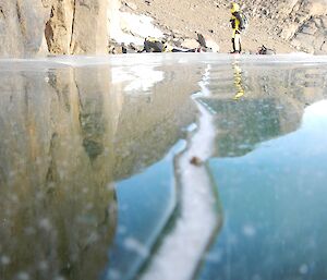 A low angle photo of an expeditioner reflected in the surface of an ice lake near Rumdoodle