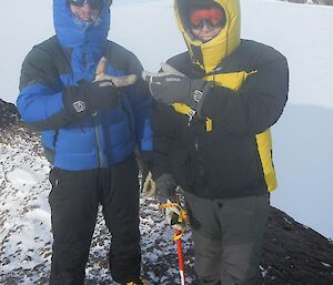 Two expeditioners standing on a peak inexplicably pointing at each other.