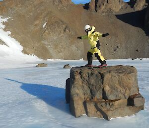 Expeditioner on rock in the middle of a frozen lake practising yoga