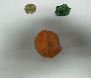 The Mawson green diamond next to a one dollar coin and a cross section of carrot, showing that the green diamond is larger than a one dollar coin.