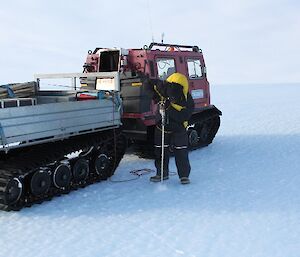 Expeditioner drilling hole in the ice before placing cane