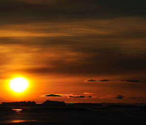 Bright yellow sun just above the horizon shrouded with a red haze reflecting of clouds