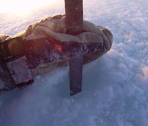 A gloved hand holds a ruler vertically into a 5cm wide drill hole in the sea ice