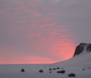 The pink sky before sunrise with a mountain in teh background and ice in the foreground