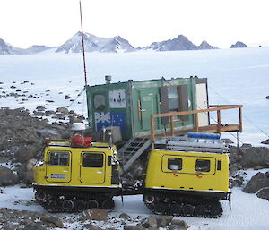 An all terrain vehilce and the green field hut in the foreground with mountain peaks dusted with snow in the background