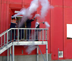 A cloud of vapour produced by 4 expeditioners standing on the landing of a red building after throwing containers of boiling water into the cold air