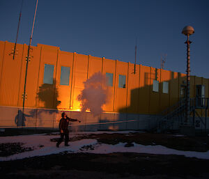A reflection of an expeditioner and the vapour cloud reflected onto the yellow Operations Building