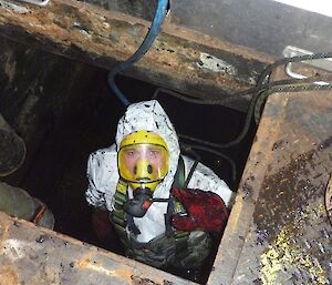 An expeditioner wearing Breathing Apparatus getting the last of the sludge out of the tank
